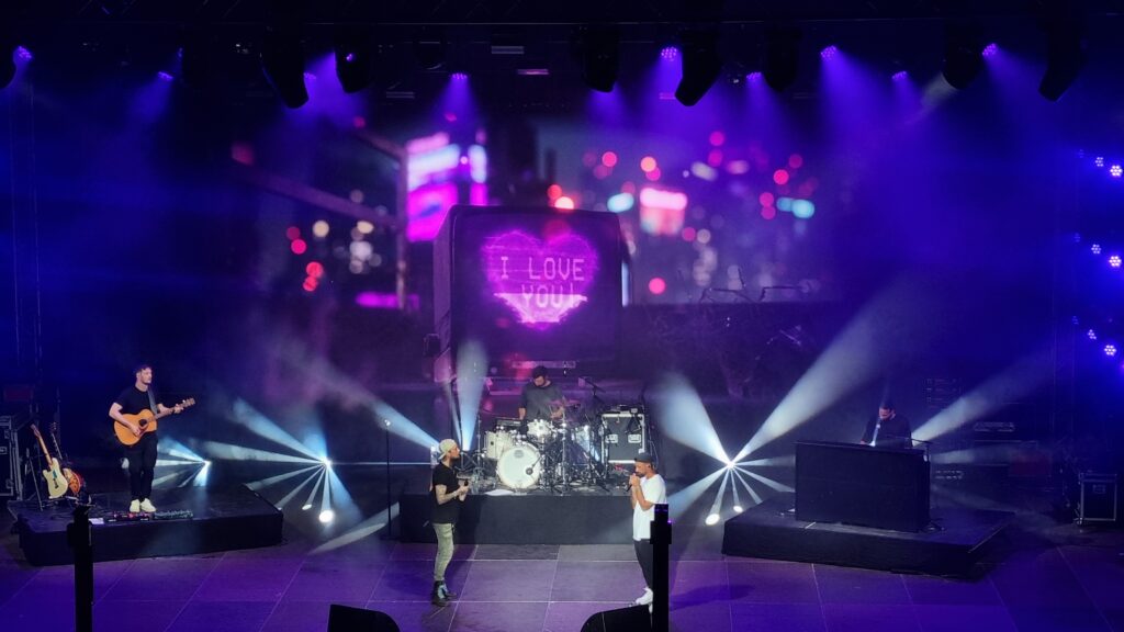 Professionelle Bühnenbeleuchtung von Luminar Design verleiht diesem Livekonzert eine magische Atmosphäre. Die perfekt choreografierte Lichtinstallation mit präzisen Spotlights und atmosphärischen lila-pinken Farbverläufen unterstreicht die Emotionalität der Performance. Erleben Sie, wie Luminar Design durch innovative Lichtkonzepte unvergessliche Konzerterlebnisse schafft und Künstler in perfektem Licht präsentiert – von der Instrumentalbegleitung bis zum Hauptakt